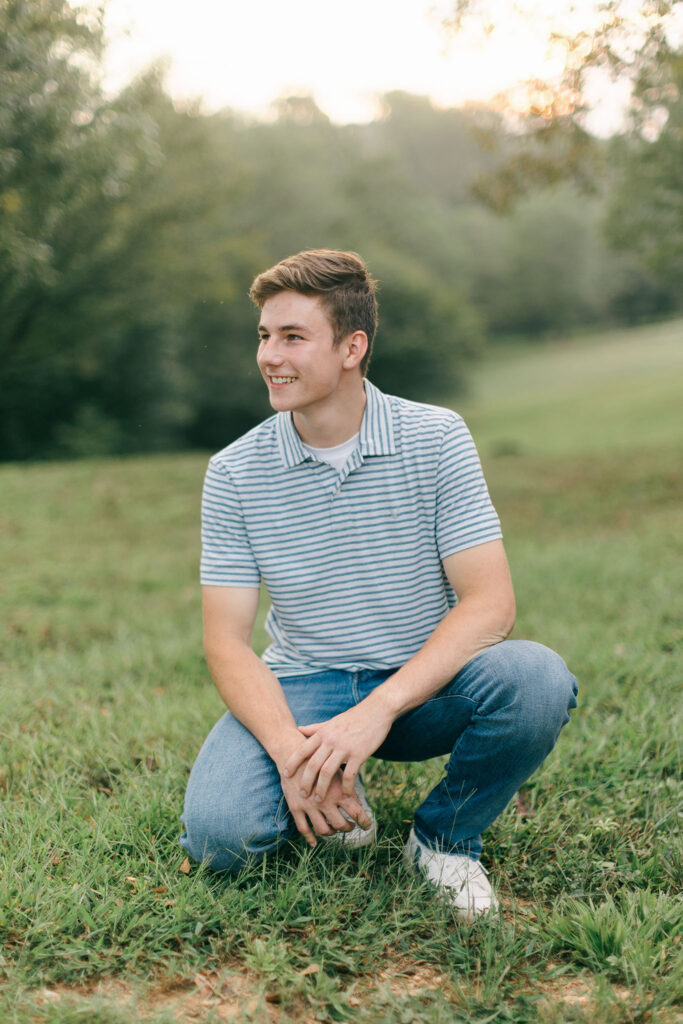 Teen boy kneeling in a field smiling during an at-home family photoshoot in Greenville SC. Dani Lacey Photographs.