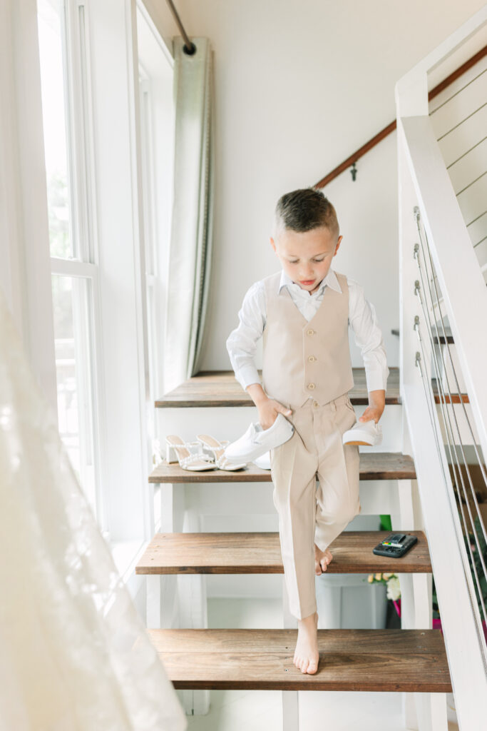 Young boy dressed for a wedding walking down stairs while holding dress shoes.