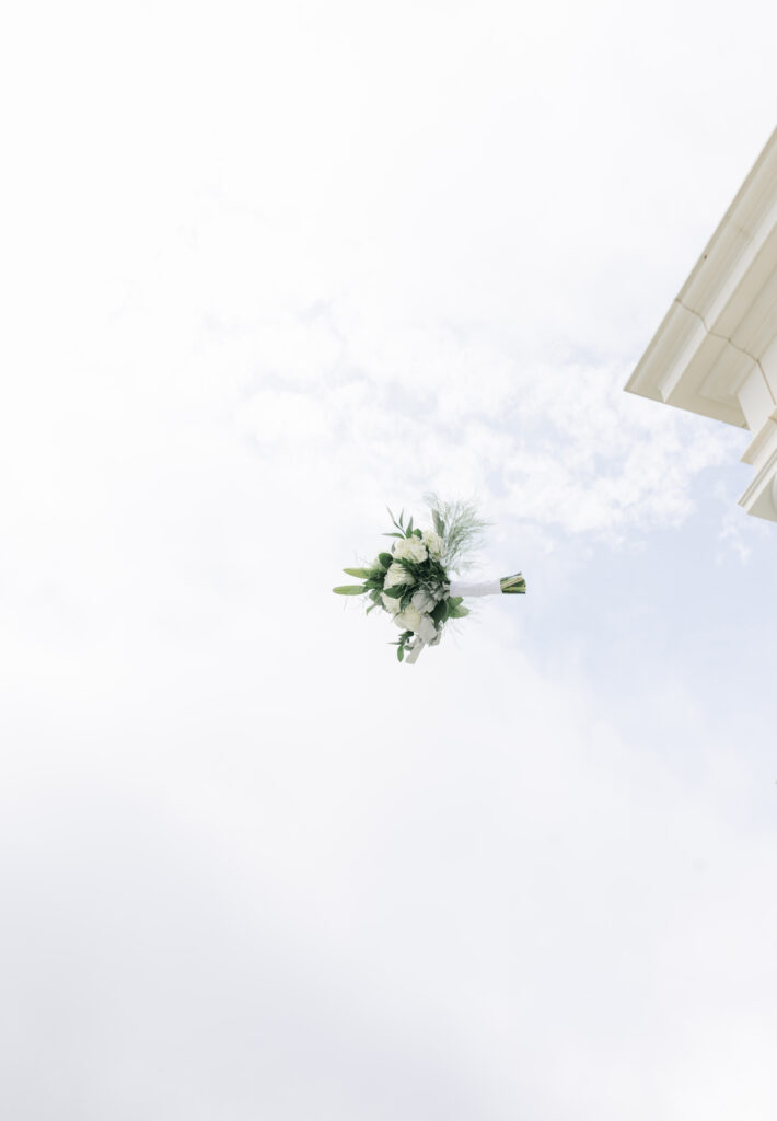Wedding bouquet tossed into the air against a bright sky.