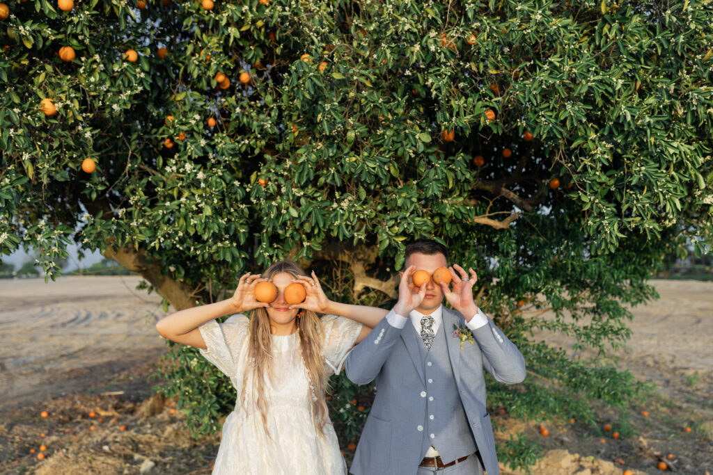 Couple playfully holding oranges during an orchard wedding session captured by a South Carolina photographer.