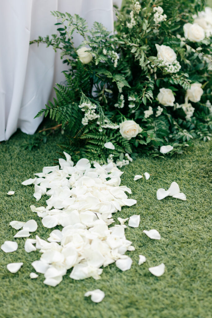 White rose petals scattered along a ceremony aisle with lush greenery, photographed by a South Carolina wedding photographer.