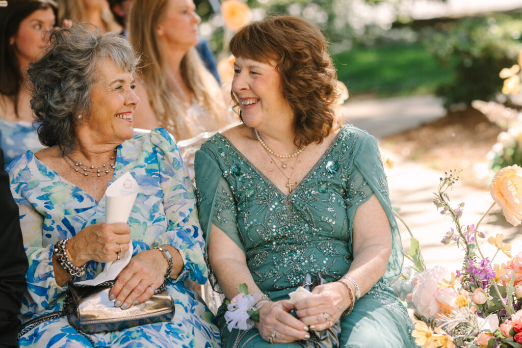 Two mothers seated during a wedding ceremony, sharing a quiet smile in South Carolina.