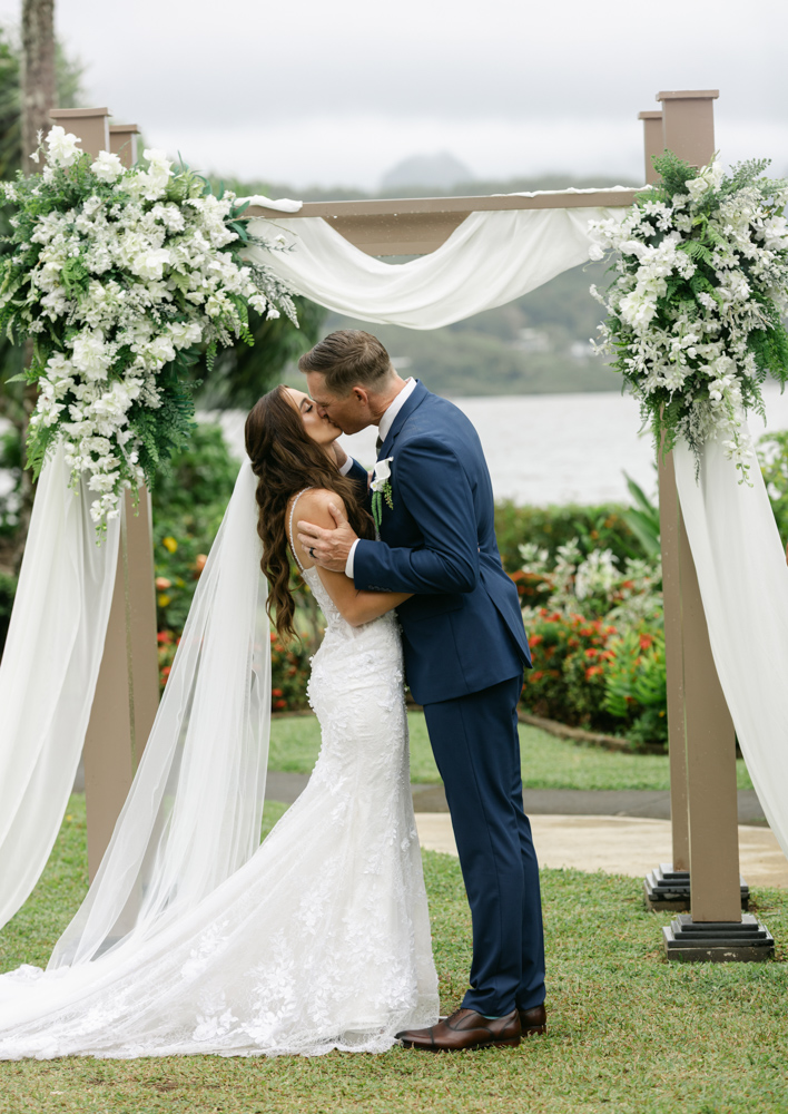 Bride and groom kissing beneath floral arch