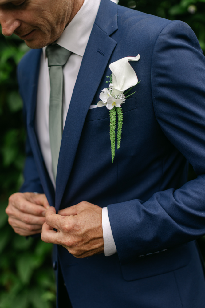 Groom adjusting blue suit jacket and boutonniere