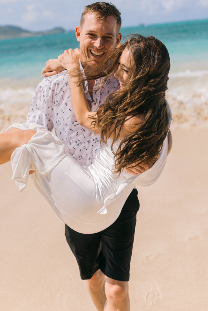 Groom carrying bride along an Oahu beach